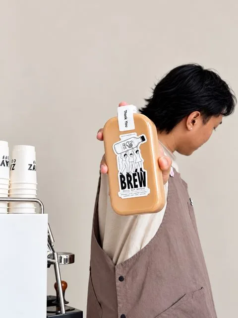 A barista holding up a bottle of Zayn Coffee Spanish latte beside the coffee bar