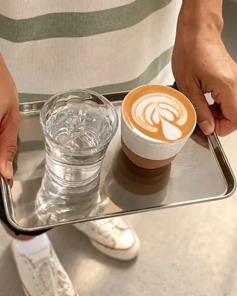 A cortado with latte art and a glass of water served on a steel tray at Zayn Coffee