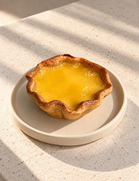 An Egg Tart with a golden custard filling on a cream plate in sunlight