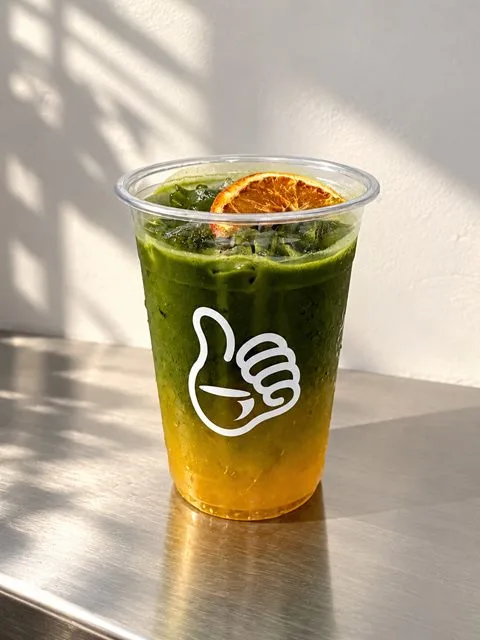 Matcha Orange, green matcha over orange with a dried orange slice, in a Zayn Coffee cup on a steel counter