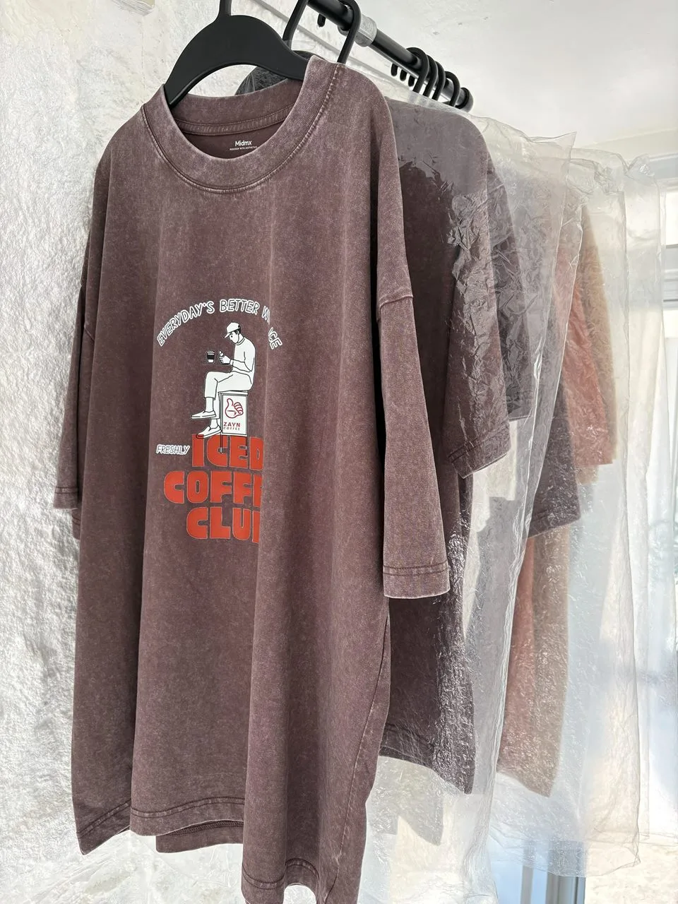 Zayn Coffee T-shirts on hangers, the front one printed with an Iced Coffee Club graphic featuring a Zayn Coffee cup