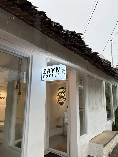 The entrance of Zayn Coffee beneath its thatched roof, with the lit ZAYN COFFEE sign